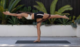 Person performing a yoga pose on a mat with plants in the background